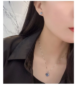 Close-up of heart-shaped blue crystal pendant and matching earrings worn by a model
