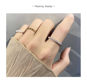 Dettaglio di anelli con perle e sfere metalliche indossati per un look a strati