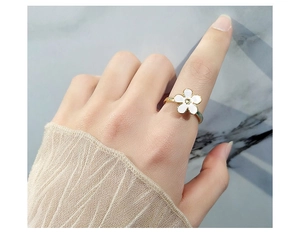 Detail shot of a rotating golden flower ring with white enamel petals on a model's finger