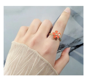Close-up of a rotating orange enamel flower ring with a crystal center on a golden band