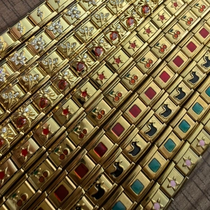 Detailed close-up of 18K gold Italian charm links with zircon insects and colorful patterns