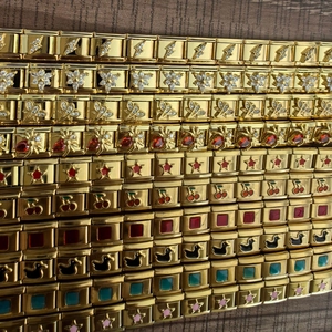Macro detail of various 18K gold Italian charm links with zircon and enamel patterns