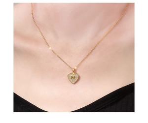 Detail van 18K vergulde hartketting met letter M en zirkoon op een vrouwelijke nek