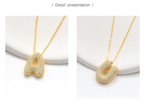 Detail view of gold bubble letter pendants A and U encrusted with white cubic zirconia