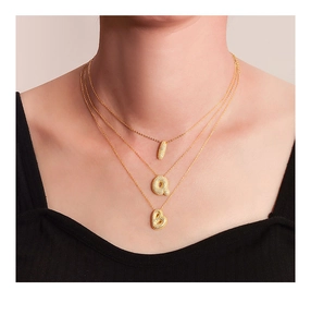 Close-up of layered gold initial necklaces with pavé cubic zirconia Q and B letter pendants