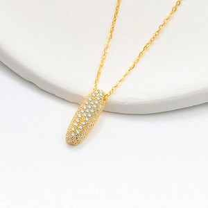 Macro shot of gold-plated capsule pendant necklace featuring sparkling white zircon stones