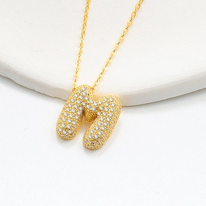 Macro shot of gold bubble letter M necklace pendant paved with shiny zircons