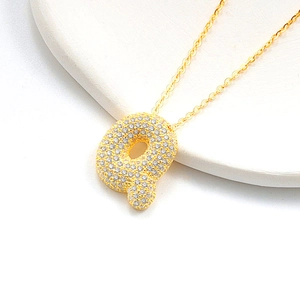 Close-up of golden bubble letter q necklace pendant with sparkling zircon gemstones