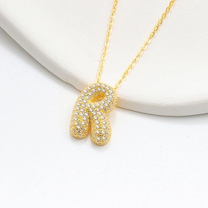 Detailed macro view of gold letter R bubble pendant with sparkling pavé stones on a chain