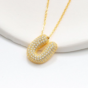 Detailed close-up of golden U-shaped pendant necklace with cubic zirconia micro-paving