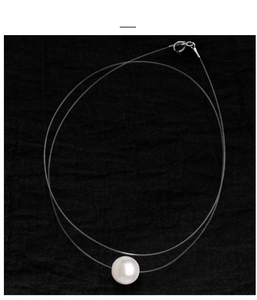 Detail of single white pearl pendant on transparent fishing line with silver metal clasp