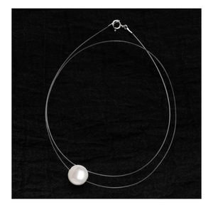 Detailed macro view of a single round pearl pendant on a clear invisible fishing line