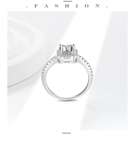Detailed view of an emerald cut moissanite ring with halo stones on a white stand