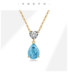 Detail of teardrop blue gemstone pendant with heart-shaped zircon on golden necklace
