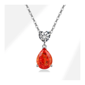 Macro detail of silver necklace with heart-shaped stone and teardrop red zircon pendant