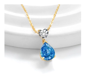 Macro shot of gold necklace featuring heart and pear-cut blue crystal drop pendant