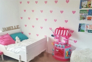 Pink heart-shaped wall stickers arranged in a pattern on a cozy nursery room wall