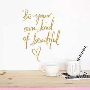 Détail de l'autocollant mural doré 'Be your own kind of beautiful' avec un cœur