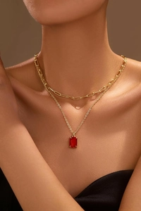 Close-up of layered gold paperclip chain necklace with a red rectangular gemstone pendant