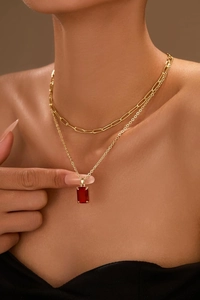 Close-up of layered gold paperclip chain and faceted red gemstone pendant on neck
