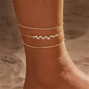 Close-up of triple layered gold beaded anklets with marquise zircon leaves on sand
