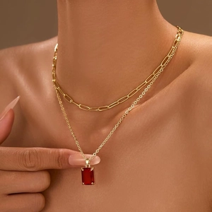 Double-layered gold paperclip chain necklace with a vibrant red rectangular crystal pendant