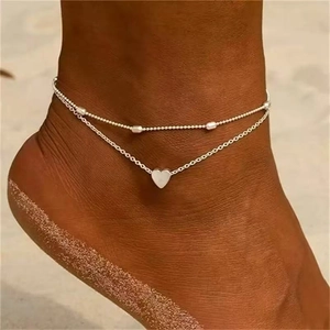 Detail of silver heart anklet with beaded double-layer chain worn on a beach ankle