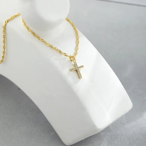 Elegante collana a croce dorata con zirconi cubici su espositore per gioielli bianco