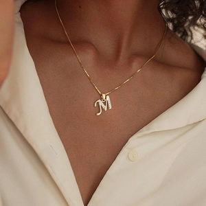 Elegant gold letter M pendant necklace with sparkling stones on model's neck