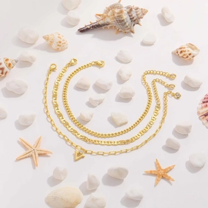 Three-piece golden Cuban ankle bracelet set with V-pendant on beach stones background