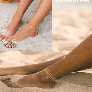 Gold double-layer Cuban link ankle bracelet with letters K and M on a beach setting