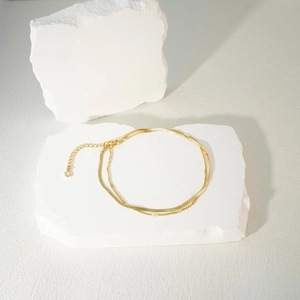 Elegant layered 14K gold stainless steel anklet with snake and curb chain on white stone