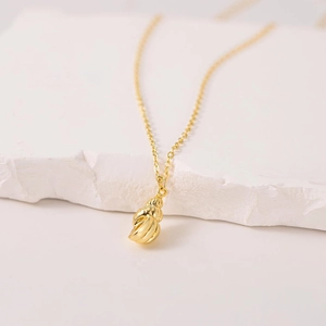 Gold conch shell pendant necklace with spiral texture on white stone background