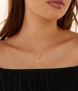 Detailed view of a gold cross and alphabet pendant necklace on a female neck