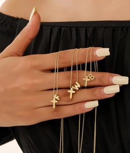 Detailed close-up of golden alphabet and cross pendant necklaces on person