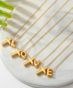 Detailed close-up of gold cross and letter pendants on elegant marble display