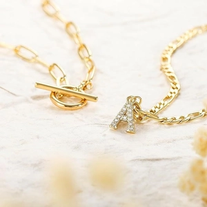 Layered gold necklace with A-letter zircon pendant and toggle clasp on stone texture