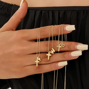 Polished gold cross and alphabet letter pendant necklace shown on a model