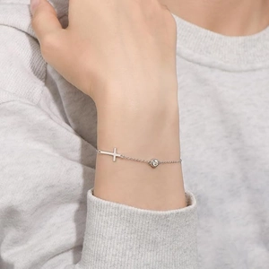 Minimalist silver chain bracelet with small cross pendant and zircon on a gray sweater