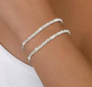 Nahaufnahme gestapelter silberner Glitzerarmbänder mit Mikro-Pavé-Kristallen am Handgelenk