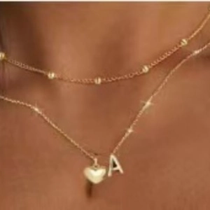 Double-layered golden necklace with letter A pendant and heart charm on beaded chains