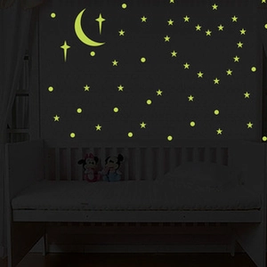 Glow in the dark wall stickers featuring moon and stars above a crib in a dark room