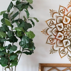 Detail eines braunen Mandala-Lotos-Wandaufklebers auf weißer Wand mit grüner Zimmerpflanze
