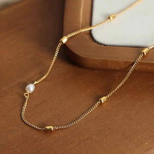 Gold plated titanium necklace with freshwater pearl pendant on a warm wooden surface