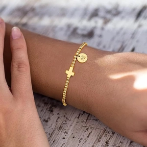 Nahaufnahme eines goldenen Perlenarmbands mit Kreuz und Buchstaben-M-Anhänger