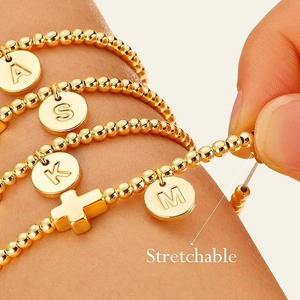 Dehnbares goldenes Perlenarmband mit personalisierten Buchstaben und Kreuzanhänger