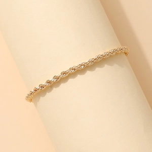 Elegante tobillera de cadena de cuerda trenzada dorada en un soporte estético beige