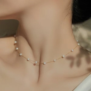 Minimalist gold chain necklace with delicate white pearls worn on a woman's collarbone
