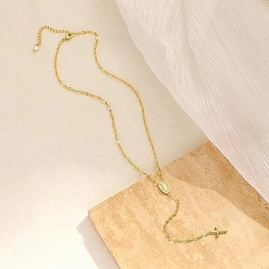 Golden crossbody necklace with Virgin Mary medal and cross pendant on stone background