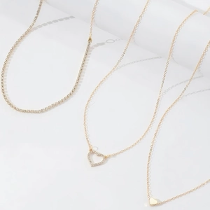 Détail de colliers dorés avec chaîne tennis étincelante et pendentifs en cœur sur décor blanc